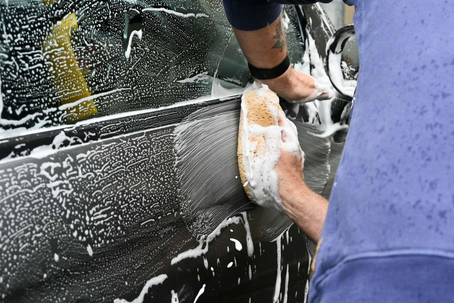 Hand washing a car door with a soapy sponge