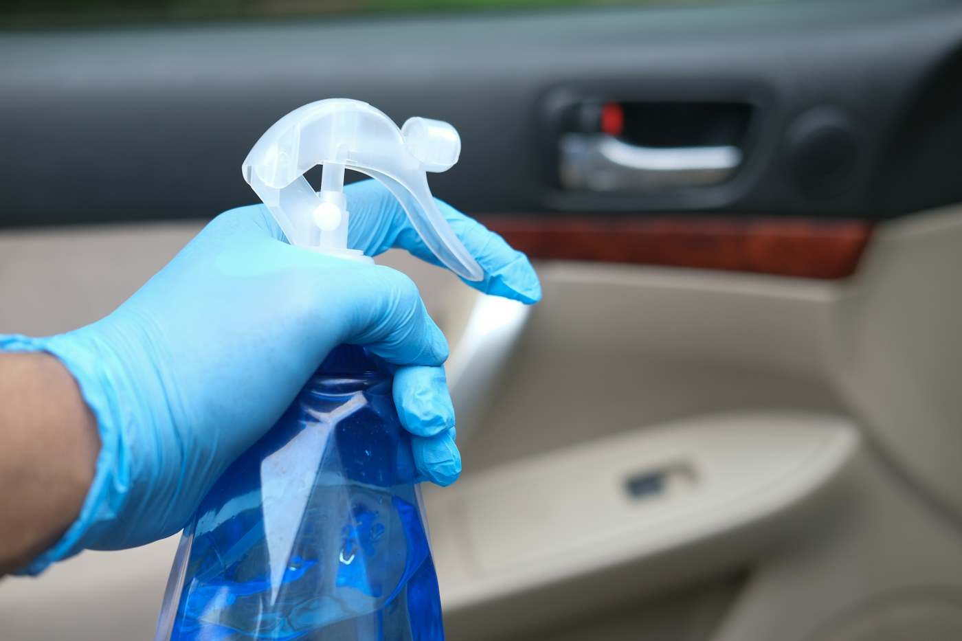 Gloved hand spraying cleaner on a car door trim