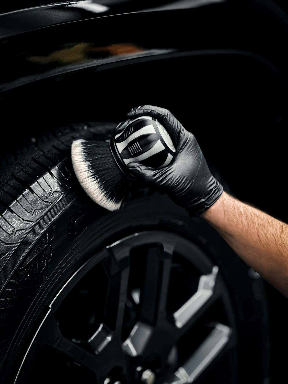 Gloved hand detailing a tyre with a soft brush